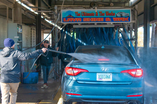 Soft cloth employees pre-wetting a car before it enters the car wash.