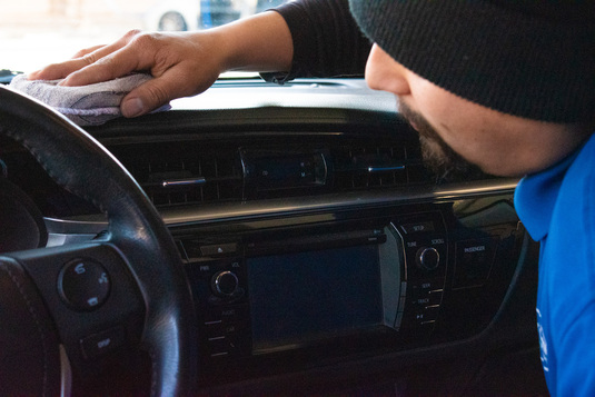 Soft cloth employee detailing the dash of a customers car.