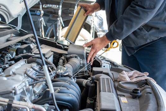 Hands of a technician changing the air filter on a car in for service.